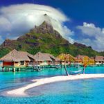 a group of houses on stilts in a body of water with Bora Bora in the background
