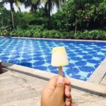 a hand holding a popsicle next to a pool