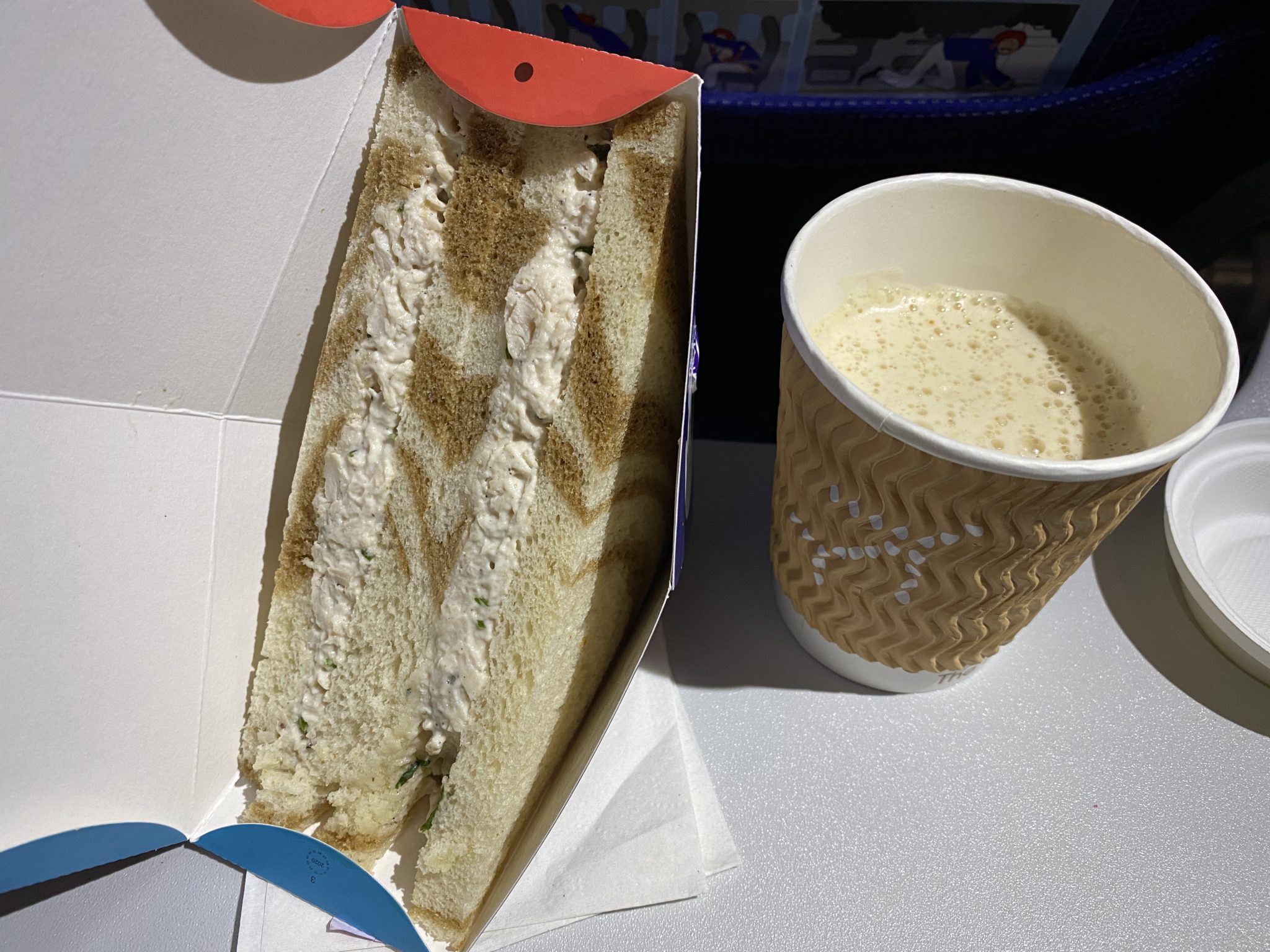 a sandwich in a box next to a cup of coffee