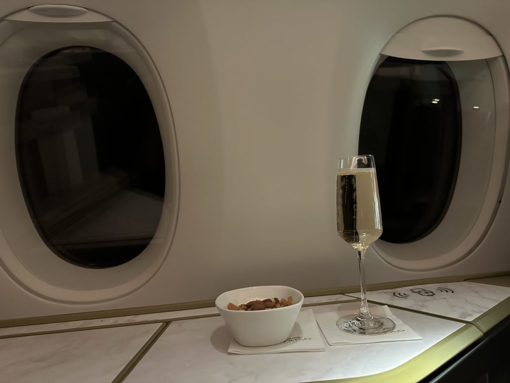 a glass of champagne and a bowl of nuts on a table in an airplane