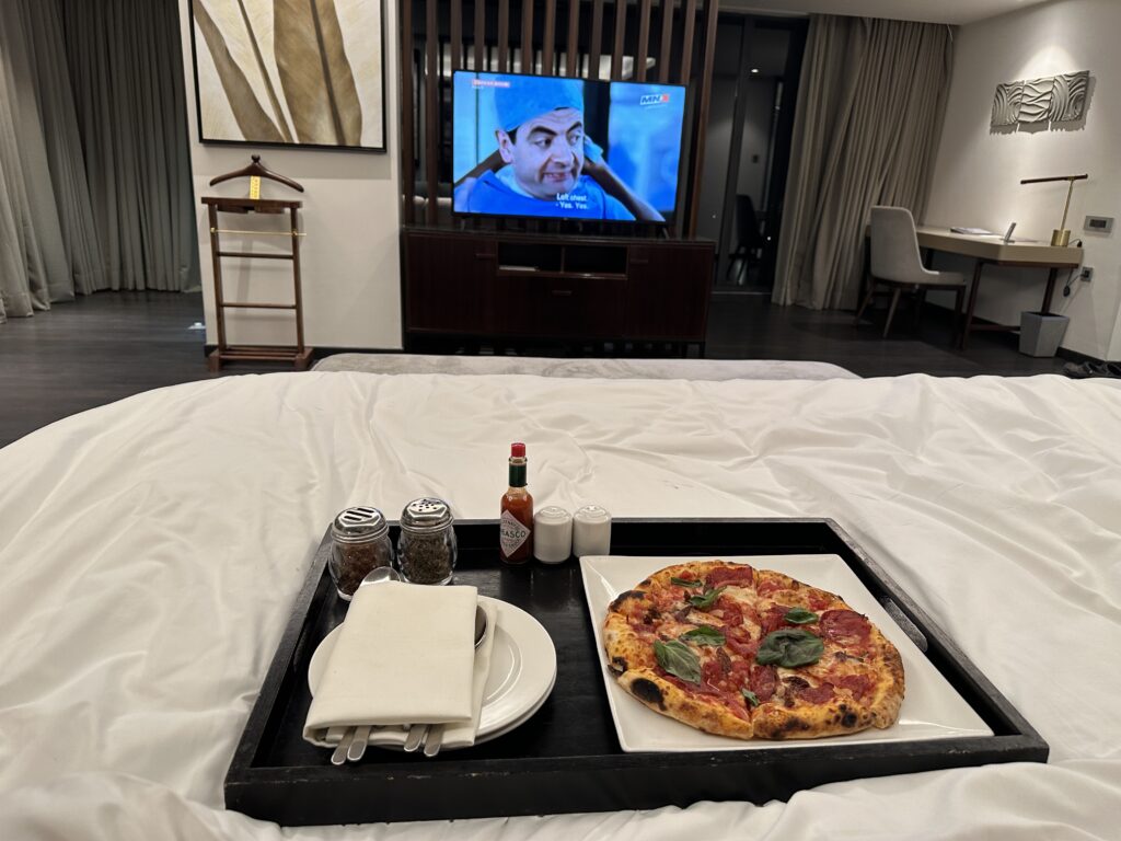 a tray of pizza and spices on a bed with a television in the background