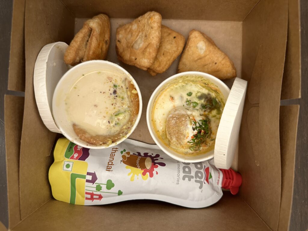 a box of food with a couple of cups of soup and some sauce