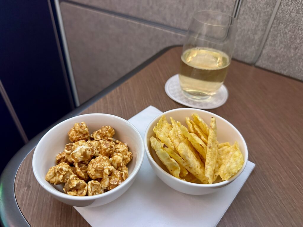 a bowl of popcorn and potato chips on a napkin next to a glass of liquid