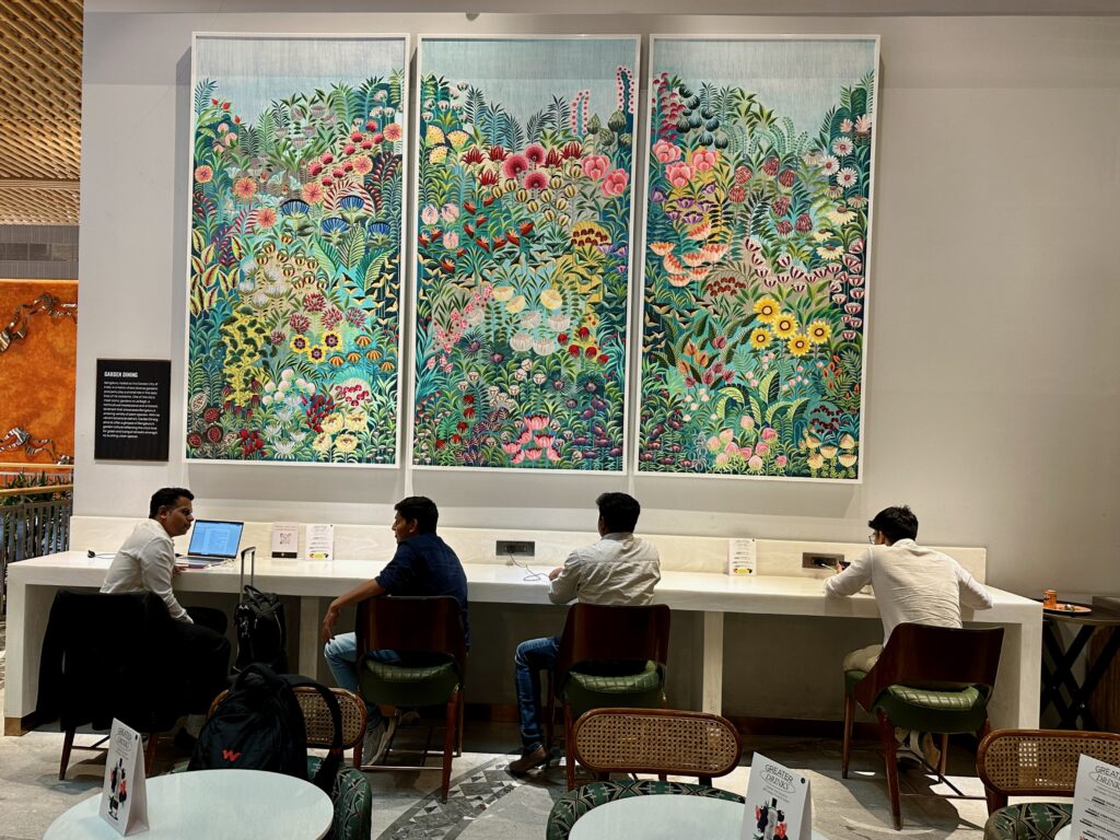 a group of people sitting at a table with a large painting on the wall