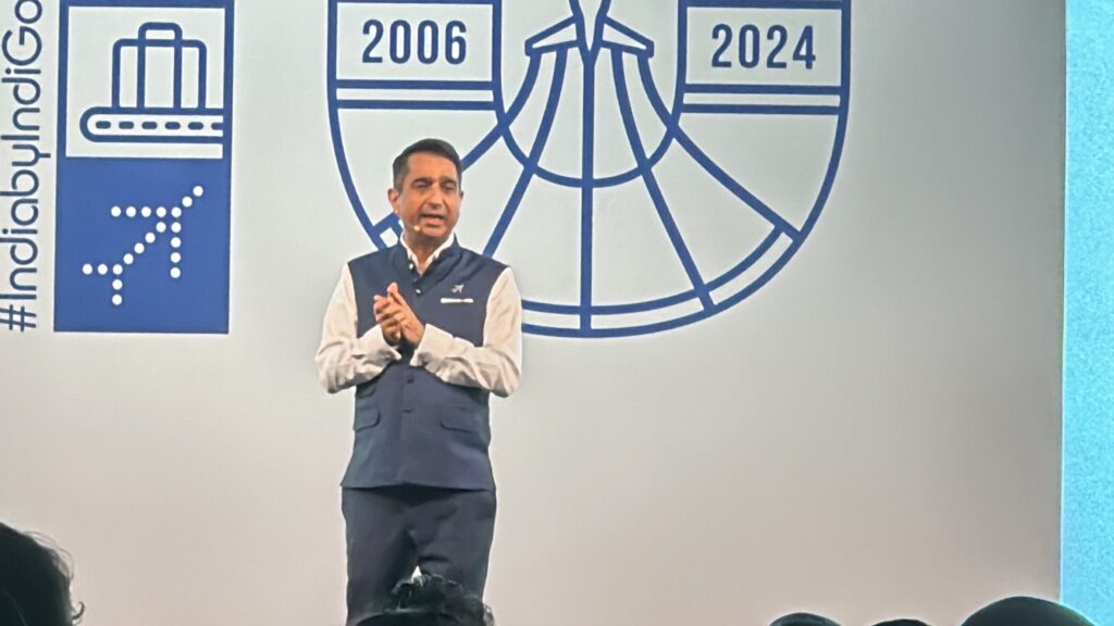 a man standing in front of a white wall with a logo on it