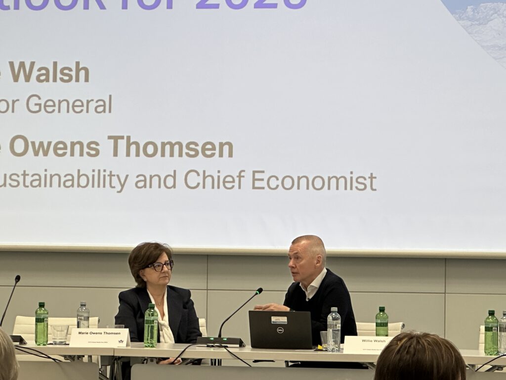 a man and woman sitting at a table with laptops and a projector screen