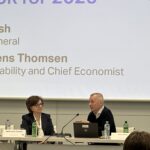 a man and woman sitting at a table with laptops and a projector screen