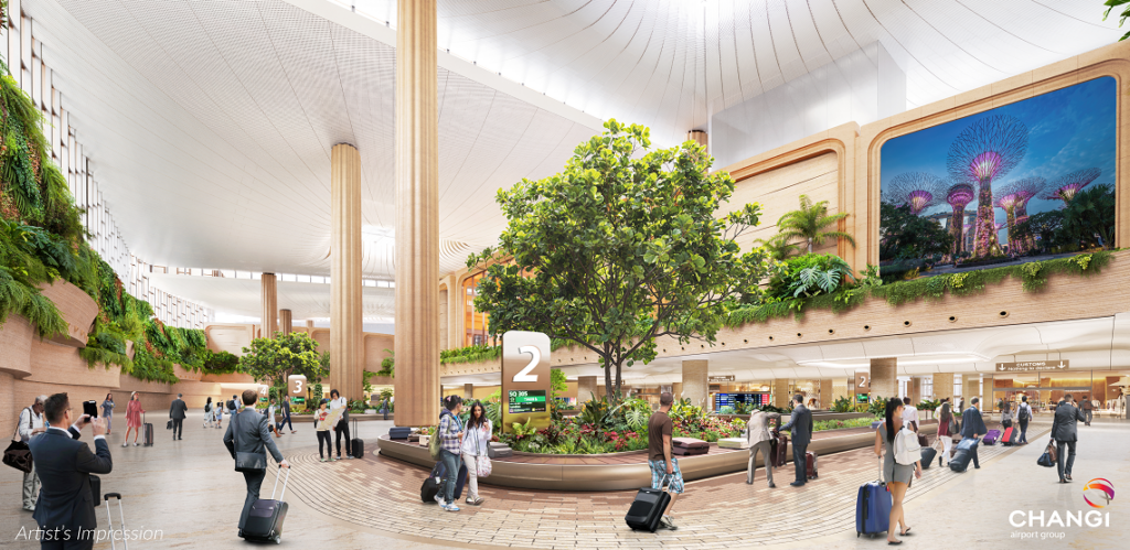 The image is an artist's impression of an airport interior. It features a spacious, modern design with large columns and a high ceiling. There are lush green plants and trees integrated into the architecture, creating a natural atmosphere. People are walking with luggage, and there are signs indicating directions. A large digital screen displays an image of illuminated structures resembling trees. The environment is bright and welcoming.