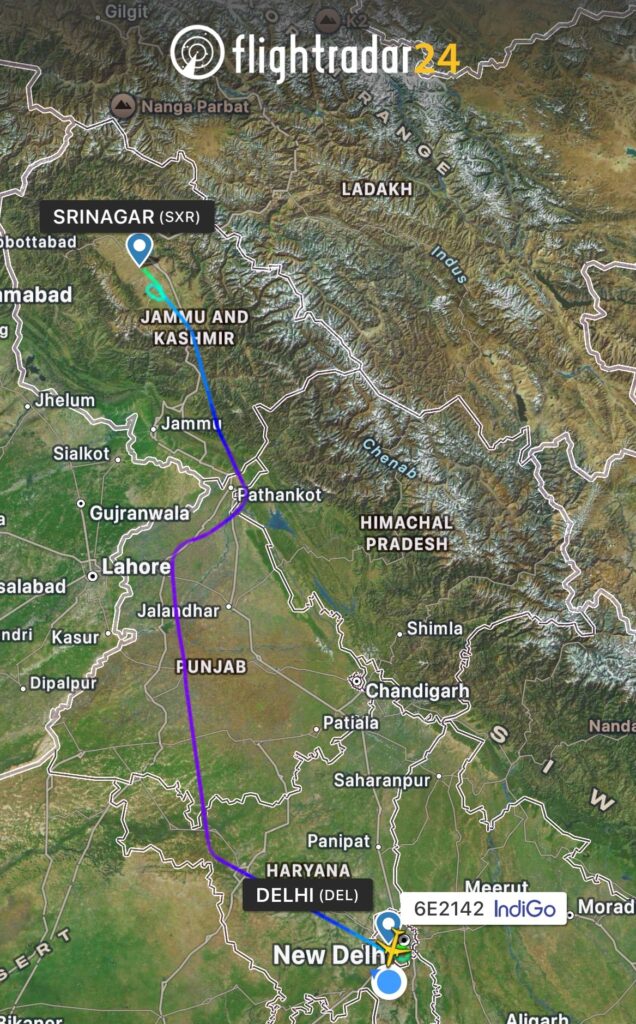 The image is a screenshot from the Flightradar24 app showing a flight path from Srinagar (SXR) to New Delhi (DEL) in India. The map highlights regions such as Jammu and Kashmir, Punjab, and Himachal Pradesh. The flight path is marked with a blue line, and the current position of the flight is indicated with a plane icon. The flight number is 6E2142 operated by IndiGo.