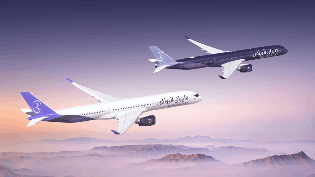 The image shows two airplanes flying above a mountainous landscape during what appears to be sunrise or sunset. The sky is a gradient of purple and pink hues. The airplanes have "Riyadh Air" written on their sides, with one plane in a white livery and the other in a dark blue livery. Both planes have purple tails with a logo.