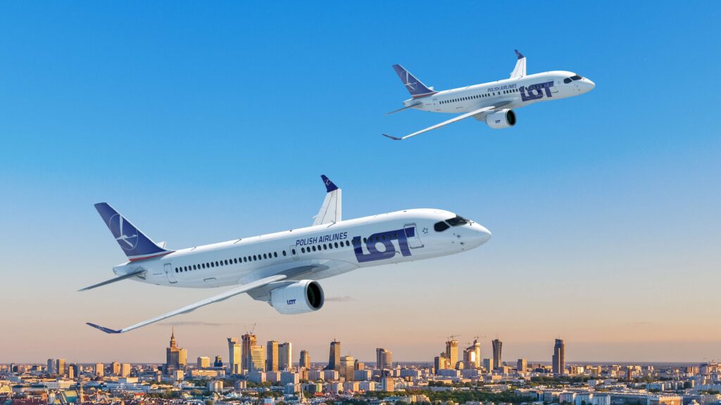 The image shows two LOT Polish Airlines airplanes flying in the sky above a cityscape. The aircraft are white with blue and purple accents, featuring the airline's logo on the tail and fuselage. The city below has several tall buildings and a clear blue sky above.