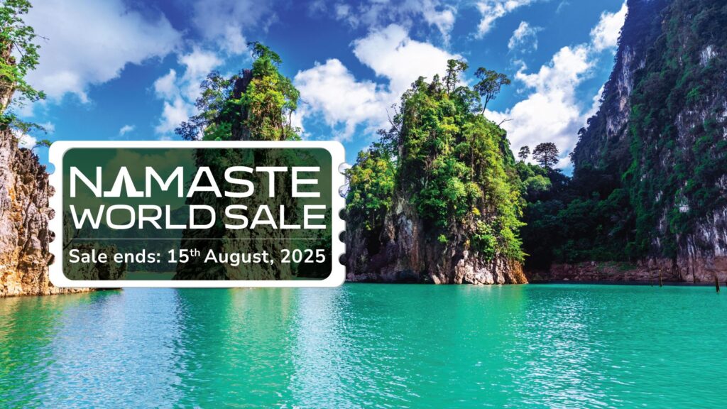The image shows a scenic view of a turquoise body of water surrounded by tall, rocky cliffs covered in lush green vegetation. The sky is blue with scattered clouds. Overlaid on the image is a promotional graphic with the text "NAMASTE WORLD SALE" and "Sale ends: 15th August, 2025" in white letters on a dark green background.