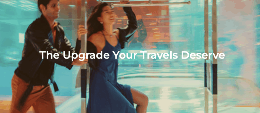 A man and a woman are joyfully running through a revolving door. The woman is wearing a blue dress, and the man is in a dark jacket and brown pants. The background is a blur of colors, suggesting motion. Overlaid text reads, "The Upgrade Your Travels Deserve."