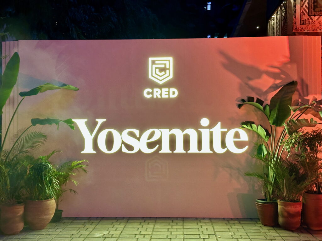 The image shows a large sign with the word "Yosemite" in bright, illuminated letters. Above it is the logo and name "CRED." The sign is surrounded by potted plants, and the area is lit with colorful lighting, creating a vibrant atmosphere.