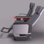 The image shows a side view of two modern airplane seats in a reclined position. The seats have a sleek design with dark upholstery and integrated headrests. The armrests feature built-in controls and a small screen. The seats are positioned on a light gray background.