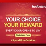 The image is a promotional banner for IndusInd Bank's "The Rewardz Festival." It has a red background with decorative patterns and text that reads, "YOUR CHOICE YOUR REWARD EVERY DOOR OPENS TO JOY." There is a button labeled "Participate Now" and a hashtag "#SpendMoreGetMore." The festival logo is in the top left corner.