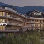 The image shows a modern, multi-story hotel building with large windows and balconies, set against a backdrop of mountains. The hotel has the name "VOCO" displayed prominently on the top. In the foreground, there are landscaped gardens with trees and shrubs. Text on the left side of the image reads "LIMITED-TIME OFFER 100% MORE POINTS." The bottom right corner has the text "voco Wugong Mountain Jiangxi."