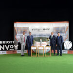 Four men in suits stand on a green carpet in front of a backdrop featuring the logos of Marriott Bonvoy and ICC, indicating a partnership. In front of them are three trophies on display. The setting resembles a sports or corporate event.