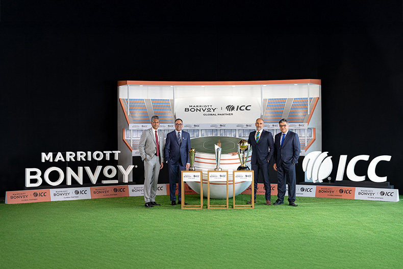 Four men in suits stand on a green carpet in front of a backdrop featuring the logos of Marriott Bonvoy and ICC, indicating a partnership. In front of them are three trophies on display. The setting resembles a sports or corporate event.