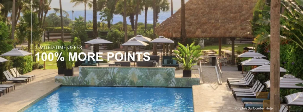 The image shows a luxurious outdoor pool area at the Kimpton Surfcomber Hotel. The pool is surrounded by lounge chairs and umbrellas, with lush greenery and palm trees in the background. A thatched-roof structure is visible, adding to the tropical ambiance. Text on the image reads "Limited-Time Offer 100% More Points."