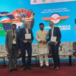 The image shows four men standing on a stage at an aviation event. They are dressed in formal attire, with two of them holding documents. Behind them is a large screen displaying graphics related to aviation, including images of aircraft, an airport terminal, and aviation professionals. The screen also features text about the event, highlighting it as Asia's largest civil aviation event. There are logos and names of partners and sponsors on the side panels.