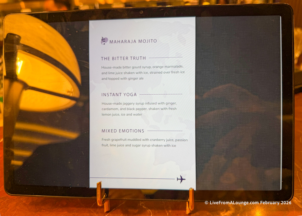 The image shows a digital menu displayed on a tablet. The menu is titled "Maharaja Mojito" and lists three drinks: 1. **The Bitter Truth**: Made with bitter gourd syrup, orange marmalade, and lime juice, shaken with ice, strained over fresh ice, and topped with ginger ale. 2. **Instant Yoga**: Made with jaggery syrup infused with ginger, cardamom, and black pepper, shaken with fresh lemon juice, ice, and water. 3. **Mixed Emotions**: Made with fresh grapefruit muddled with cranberry juice, passion fruit, lime juice, and sugar syrup, shaken with ice. The menu has a decorative airplane icon at the bottom.