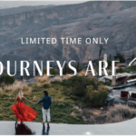 A couple is standing on the edge of an infinity pool, holding hands and looking at a scenic view of a canyon. The woman is wearing a flowing red dress, and the man is in a blue jacket and white pants. There are lounge chairs and umbrellas nearby. The text on the image reads "Limited Time Only Bonus Journeys Are Here."