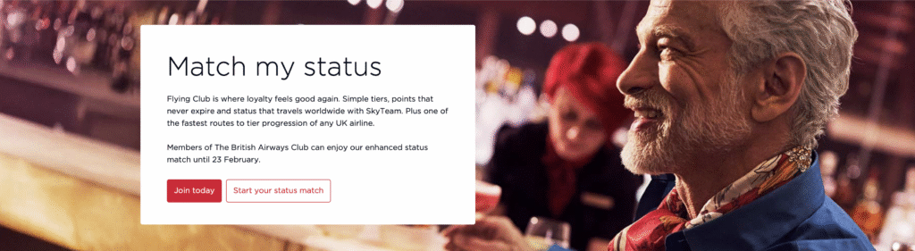 The image features a promotional banner for a loyalty program. On the left, there is text that reads "Match my status" and describes the benefits of the Flying Club, including simple tiers, points that never expire, and worldwide status with SkyTeam. It mentions an enhanced status match for British Airways Club members until 23 February. There are two buttons: "Join today" and "Start your status match." On the right, there is a smiling man with gray hair and a beard, wearing a colorful shirt and a blue jacket, in a blurred bar setting.