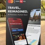 The image shows a promotional poster for "Make My Trip" featuring the Mastercard logo. The text reads "Travel, Reimagined. AI Precision. Human Soul." It displays a smartphone interface with travel-related content. The left side shows a section titled "Hey there! Let's explore," with options to view likes and saved plans, and an upcoming event in Varanasi, India. The right side highlights the "Kashi Vishwanath Corridor," a tourist attraction in Varanasi, with a description and a map. The background includes an outdoor setting with a striped umbrella and trees.