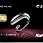 This image shows a black credit card with the logos of Axis Bank and Airtel. It features a silver abstract design in the center, a chip on the left side, and the RuPay logo on the bottom right. The card also has contactless payment symbols and a name printed on it.