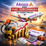 The image is a digital illustration depicting an Akasa Air airplane taking off at an airport during sunset. In the foreground, there is a barrel labeled "Jet Fuel" with fuel spilling out, a red upward arrow, and stacks of gold coins with a currency symbol. There are also Akasa Air boarding passes, a calculator, and a suitcase. The text reads "Akasa Adds Fuel Surcharges to Ticket Prices."
