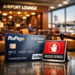 The image shows a RuPay Platinum Debit card placed next to a sign that reads "Access Denied" with a red background and a white hand symbol. In the background, there is an airport lounge with blurred figures sitting and an airplane visible through large windows.